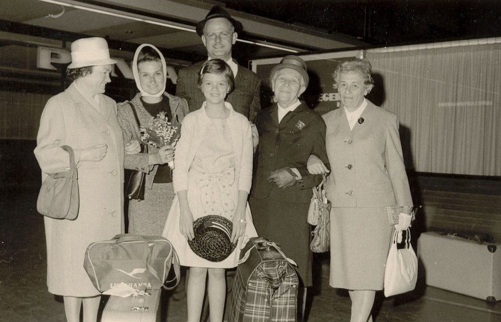 Fotografie: Empfang für Evy Woods und ihren Ehemann am Berliner Flughafen Tempelhof, von links: Hildegard Arnold, Evy Woods (mit Kopftuch), deren Ehemann Gordon, Dorothee Arnold (vorne), Elisabeth Abegg und Liselotte Pereles, 24. Mai 1964